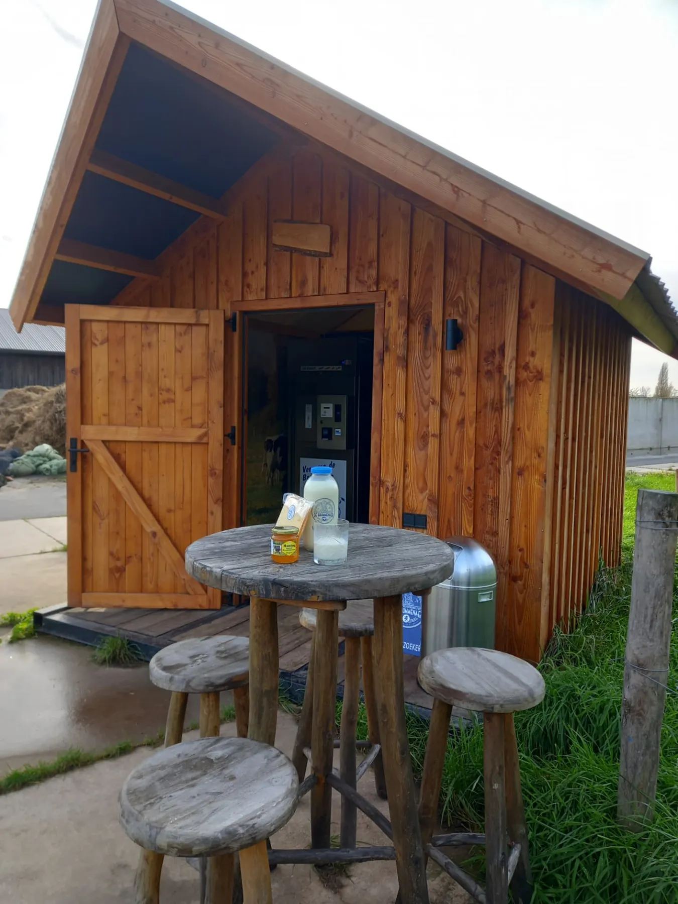 Het houten melkhuis op het erf met een fles melk en kaas op de statafel